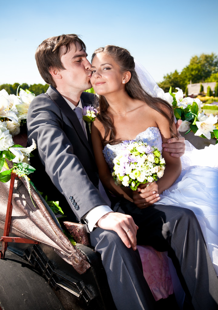 groom kissing bride in cheek on bench at park